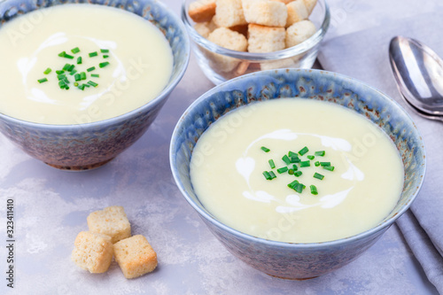 Potato leek soup in blue ceramic bowl garnished with french cream and green onion, served with croutons, horizontal