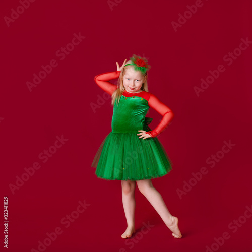 Beautiful little plump girl princess dancing in luxury green dress isolated on red background. Carnival party with costumes