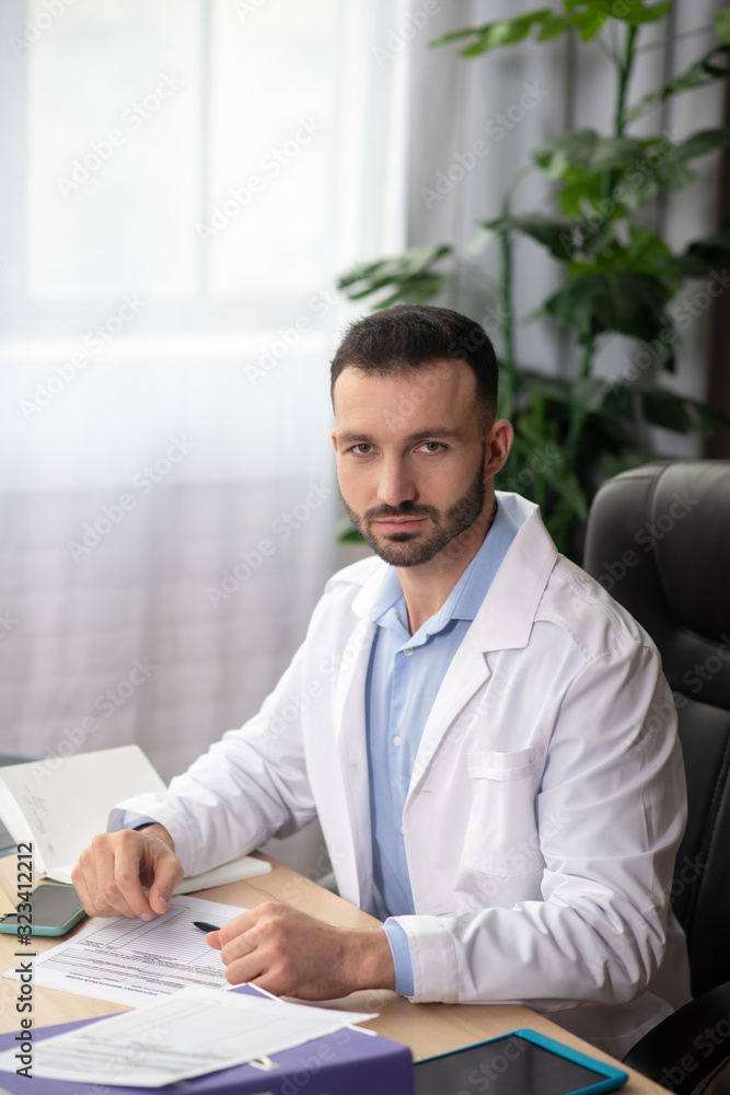 Young bearded doctor in a white robe spending his day at work Young bearded doctor in a white robe spending his day at work