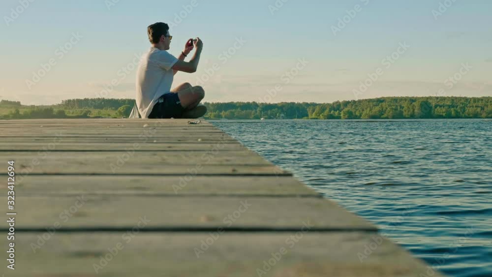 guy sits on wooden pier and takes photo of nice calm river guy sits on wooden pier and takes photo of nice calm river