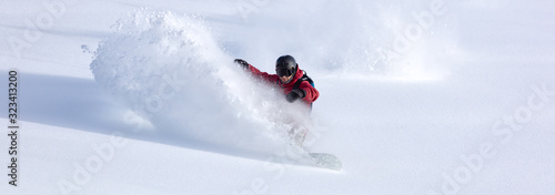 heliski snowboarding. freerider in a bright suit rides snowboarding with large splashes of snow on a sunny day. Young snowboarder. concept snowboard. big swirls of fresh snow in Good powder day