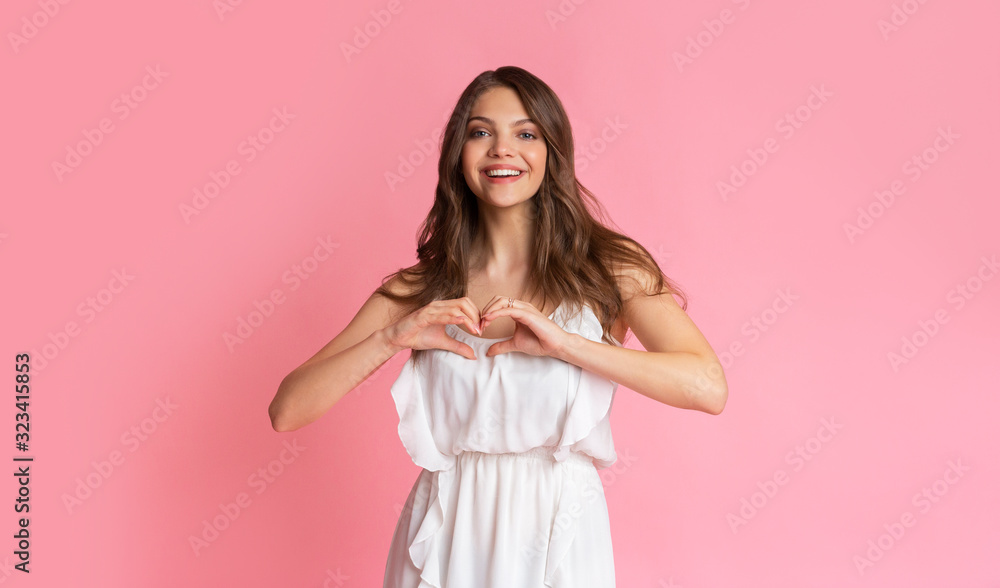 Romantic young girl shaping hands like heart, posing over pink background Romantic young girl shaping hands like heart, posing over pink background