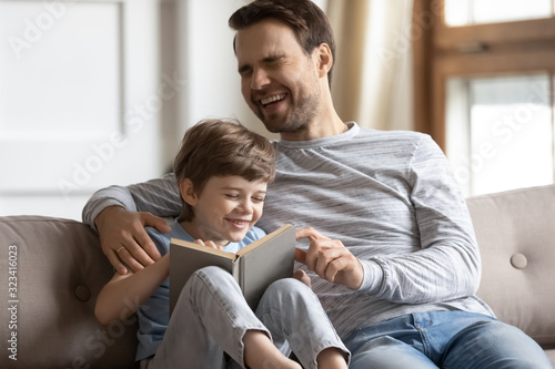 Happy little boy laughing at story, reading book with father.