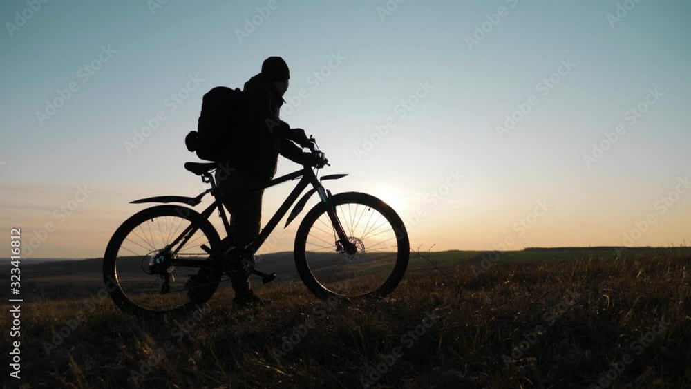The silhouette of the mountain bicycle rider on the hill with bike at sunset. Sport, travel and active life concept. The silhouette of the mountain bicycle rider on the hill with bike at sunset. Sport, travel and active life concept.