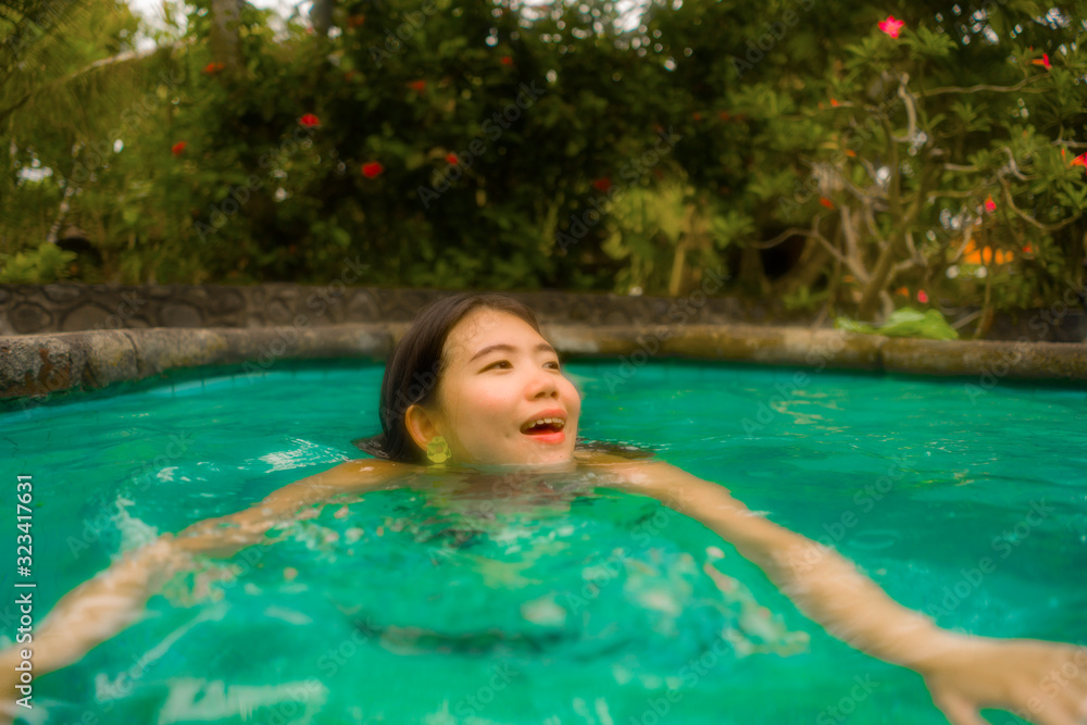holidays lifestyle portrait of young beautiful and happy Asian Chinese woman in bikini enjoying vacation trip relaxed and blissful at tropical resort swimming pool in exotic tourism concept