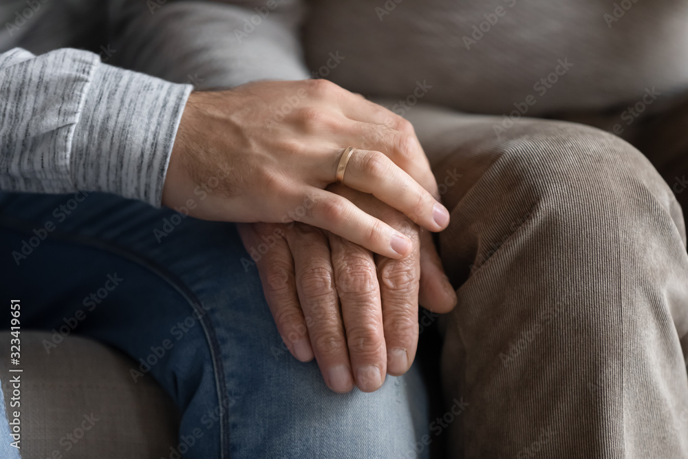 Young man put hand on wrinkled older senior fathers hand.