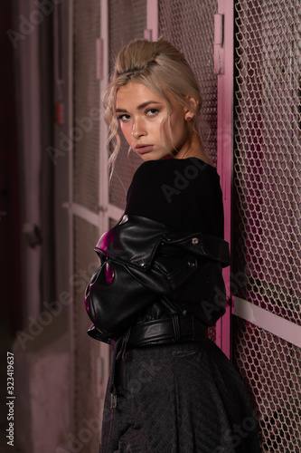 Fotografi blonde girl in a black leather jacket posing on a dark background and pink latti