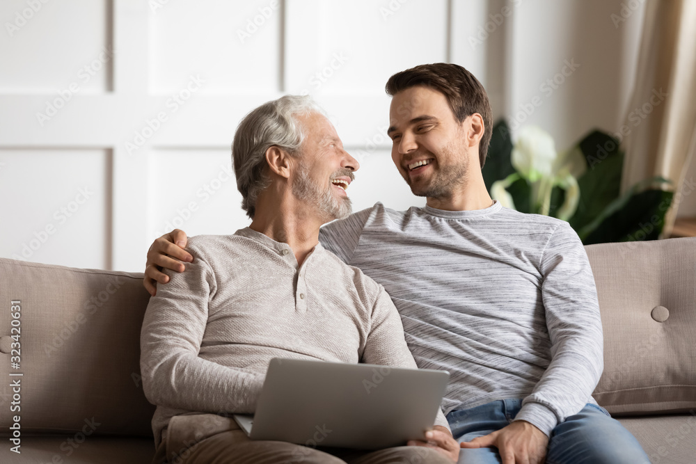 Happy elderly man holding computer enjoying fun time with son. Happy elderly man holding computer enjoying fun time with son.