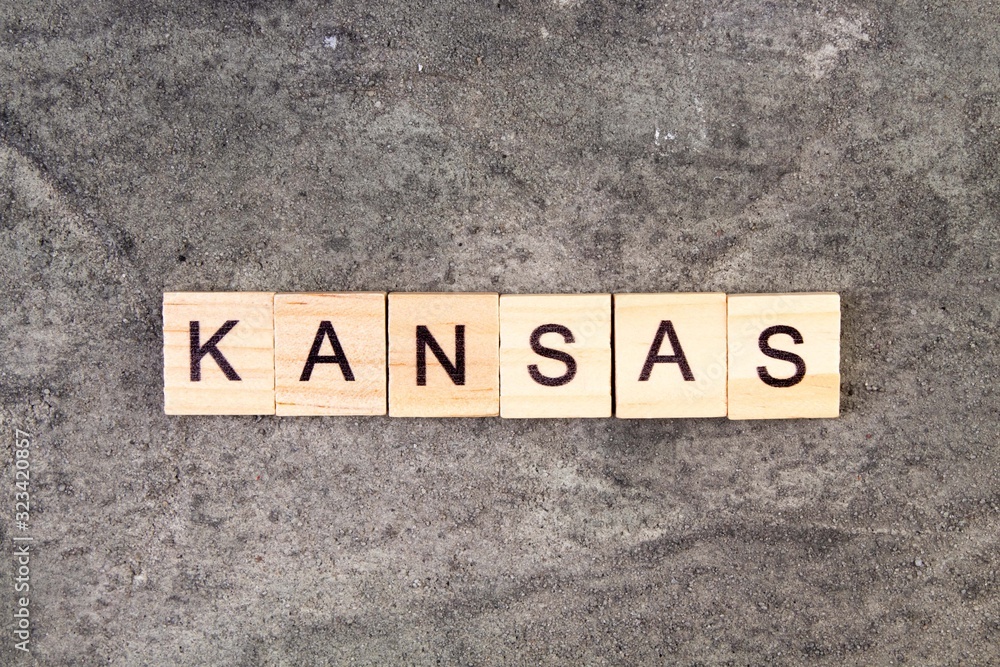 Kansas word written on wood block, on gray concrete background. Top view. Kansas word written on wood block, on gray concrete background. Top view.