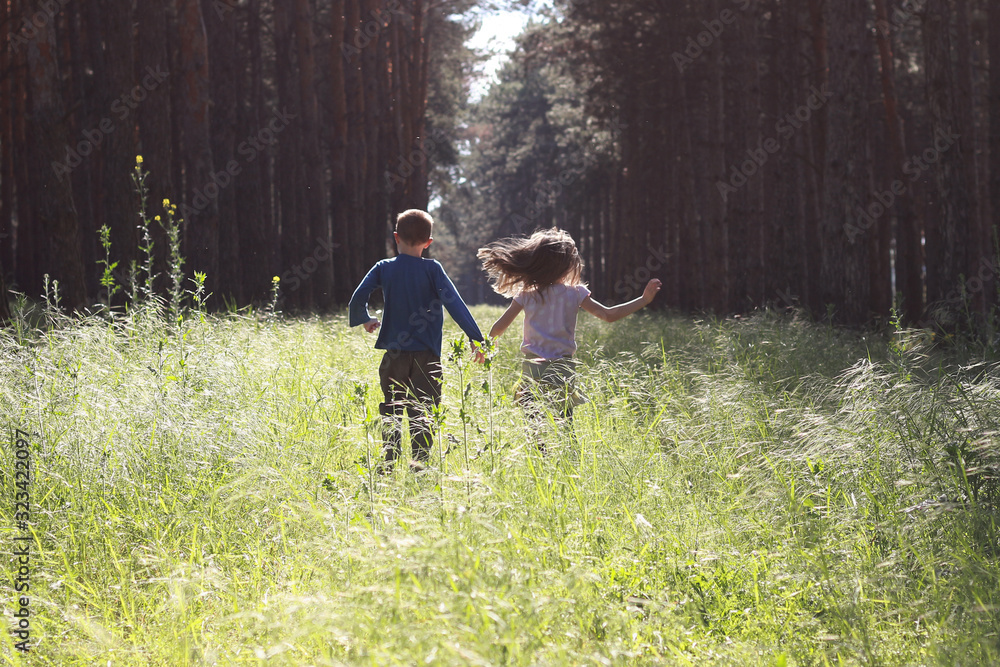 Boy and girl are running through the green forest, holding hands.
