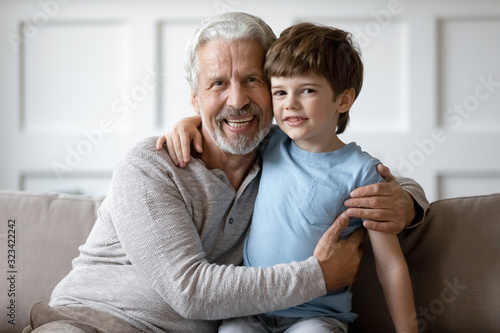 Happy middle aged grandfather embracing little schoolboy at home.