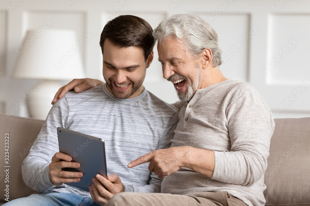 Smiling young man showing funny photo on tablet to father.