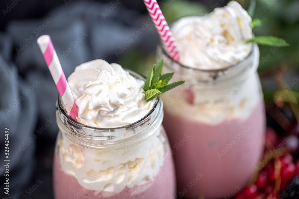 2 jars of milkshake or smoothie with cranberries, strawberries and blueberries standing on stone backdrop. 2 jars of milkshake or smoothie with cranberries, strawberries and blueberries standing on stone backdrop.
