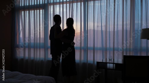 Silhouette of kissing and hug loving couple against window at sunset