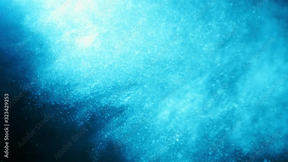 Blue glitter flying in wind. Underwater particles shining in bright spot light, shot with depth of field. Space dust beautiful bokeh abstract background Blue glitter flying in wind. Underwater particles shining in bright spot light, shot with depth of field. Space dust beautiful bokeh abstract background