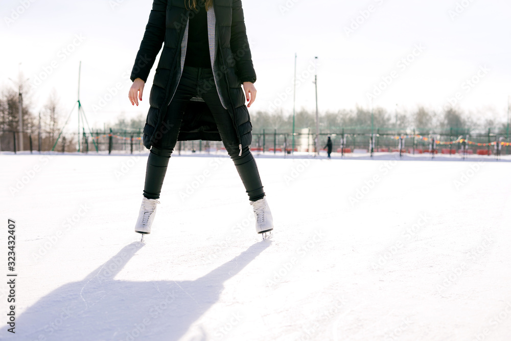 Low angle view woman skating and training with white skates on the ice area in winter day. Weekends activities outdoor in cold weather. Low angle view woman skating and training with white skates on the ice area in winter day. Weekends activities outdoor in cold weather.