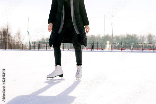 Low angle view woman skating and training with white skates on the ice area in winter day. Weekends activities outdoor in cold weather.