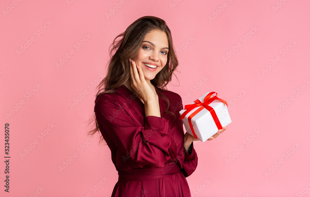 Pretty young woman holding gift box and looking at camera Pretty young woman holding gift box and looking at camera