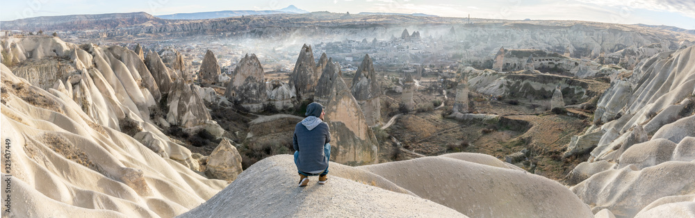 Male person low on his knees looking over the valley with Goreme town in the background. Solo exploration in Turkey. Travel destination-Cappadocia 2020.