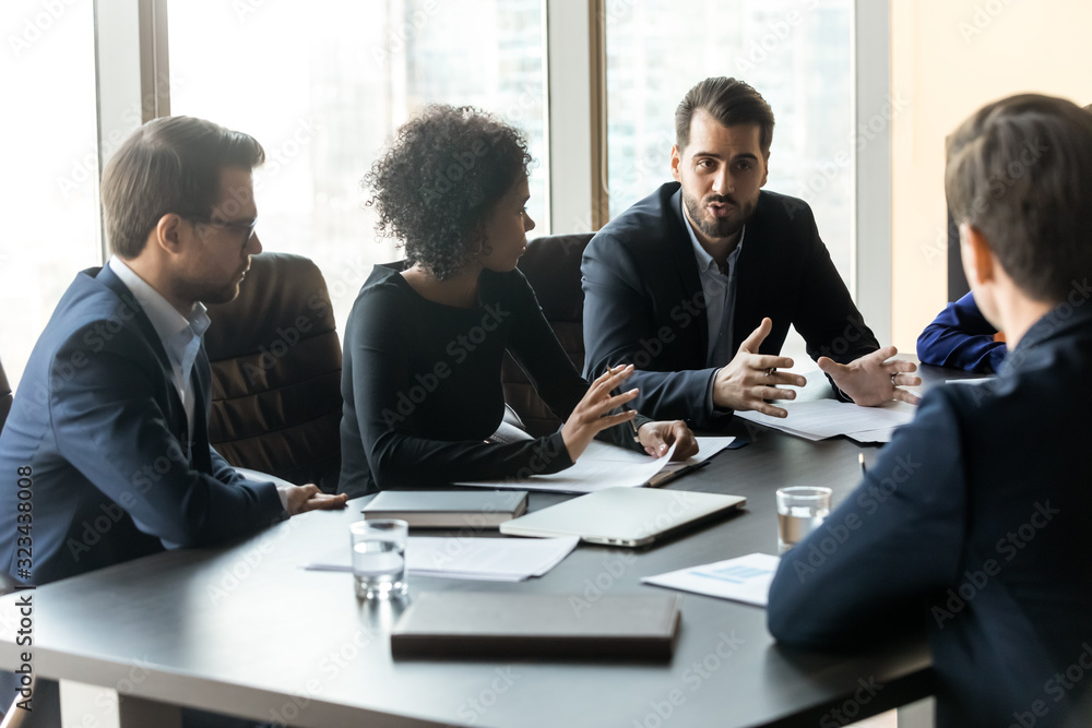 Serious businessman telling diverse employees about project sit at table. Serious businessman telling diverse employees about project sit at table.