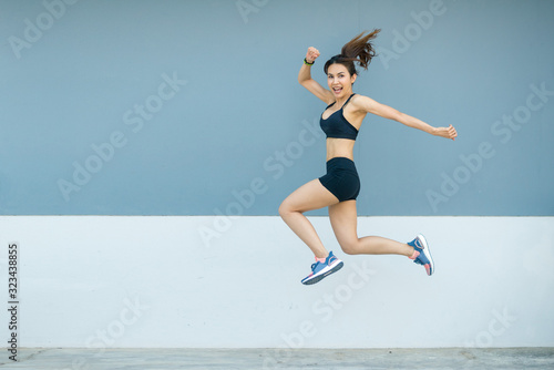 Fototapeta Naklejka Na Ścianę i Meble -  Beautiful young athletes are jumping in front of the indigo or gray and white background. She is bright and very happy.