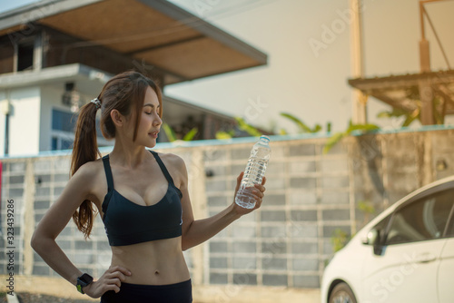 Sporty women drinks outdoor on a sunny day in front of the accommodation and she looks very bright. © Jukrachai