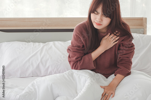 Young woman in pajamas having heart attack,Heart attack. Young woman lying in bed at home holding a hand to her chest by a sharp pain in heart.