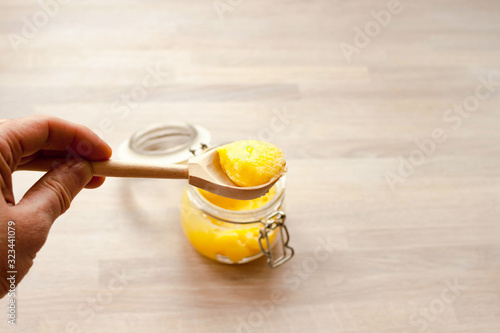 Ghee clarified butter desi in glass jar with spoon made from wood in hand. Natural wooden background