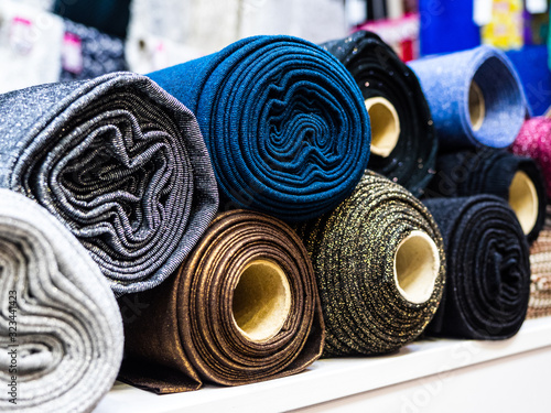 Rolls of shiny knitted fabric for sewing evening and ball gowns close-up. A selection of different beautiful fabrics for sewing fashion collections of clothing. Factory fabrics in stock