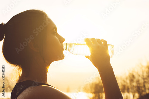 Young beautiful woman drinks water from a bottle in the sun