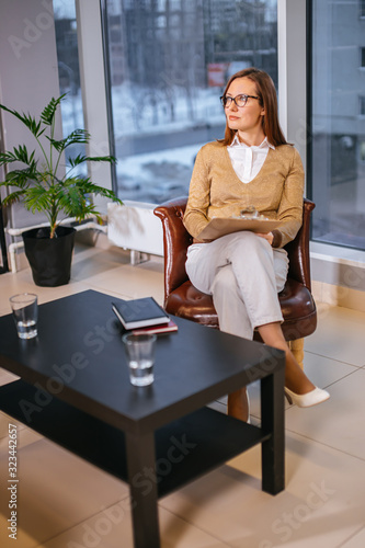 side view on seriously looking lady psychologist in eyeglasses, woman sit on leather chair in her own office and kindly look side, waiting for patients. psychology, therapy, help, people concept