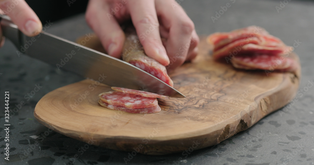 man slicing fuet sausage on olive wood board