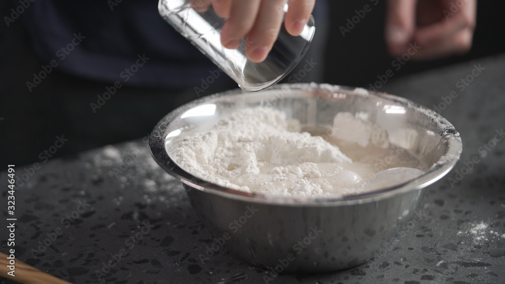 man adds wet ingredients into flour in steel bowl on concrete countertop man adds wet ingredients into flour in steel bowl on concrete countertop