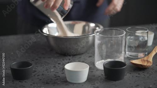 man adds dry ingredients into flour in steel bowl on concrete countertop