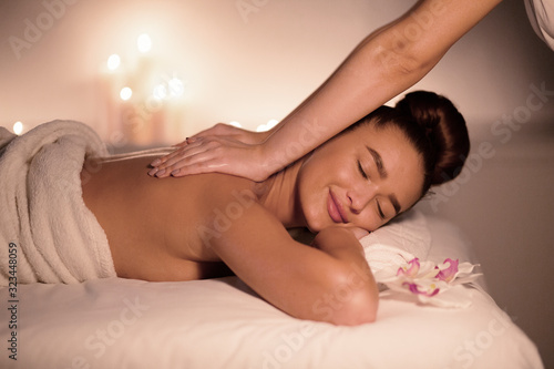 Woman receiving classical back massage with candles on background