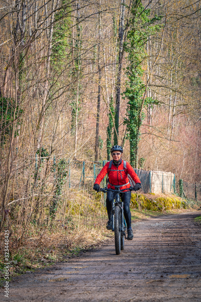 nice active senior woman riding her electric mountain bike in early spring along a little river near Stuttgart