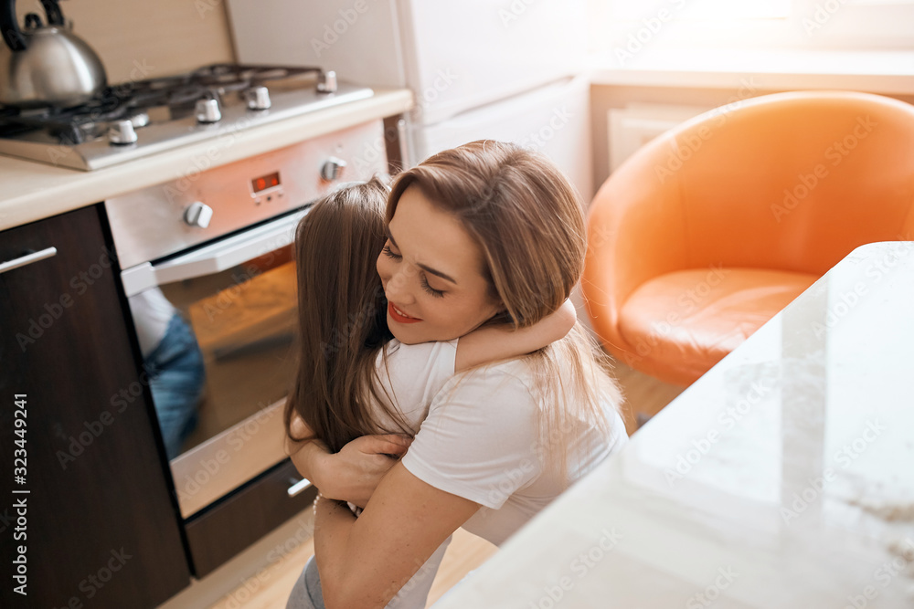 lovely kid and her mother hugging, embracing in the kitchen, expressing warm feeling and emotion. close up side view photo lovely kid and her mother hugging, embracing in the kitchen, expressing warm feeling and emotion. close up side view photo