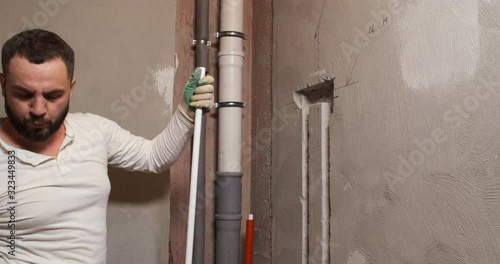 Bearded plumber cuts plastic pipes with special cutter, paves new sewer in apartment, repairs, blows off plastic shavings, construction worker, repairing leaks, updating, replacing, bathroom, sewage
