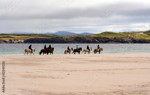 Row of horse riders on sandy beach in Ireland.