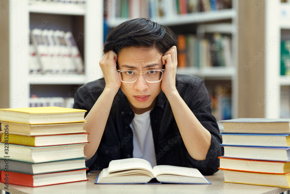 Stressed chinese guy preparing for exam in library Stressed chinese guy preparing for exam in library
