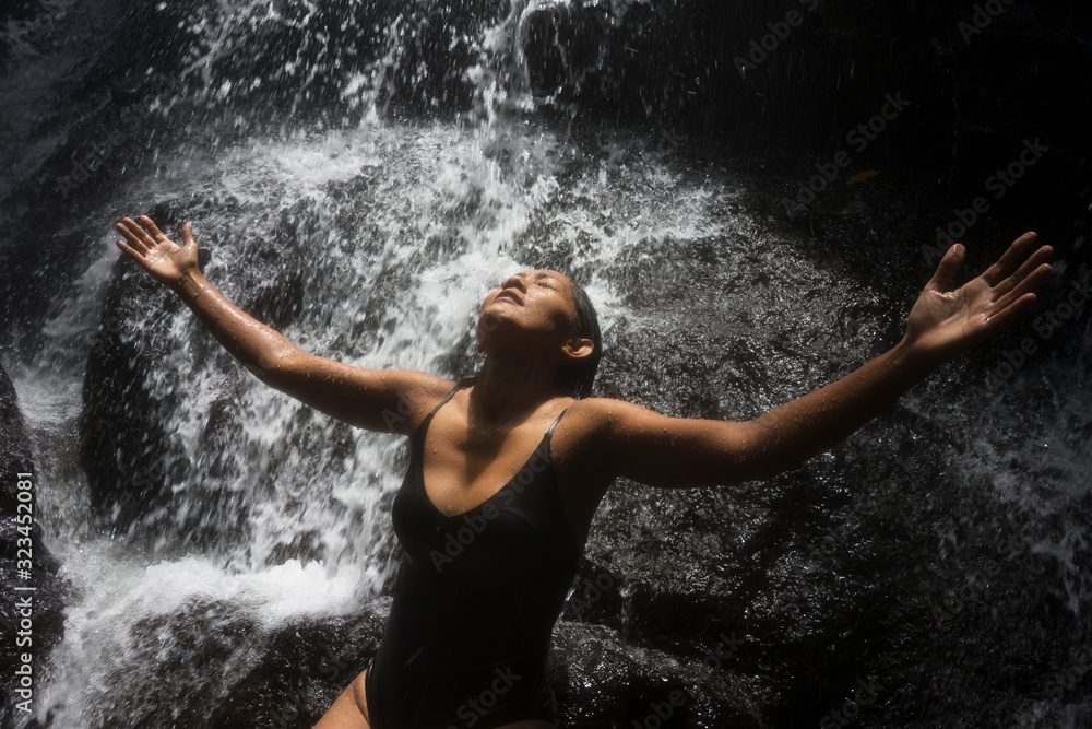 Fototapeta premium young attractive and blissful Asian Indonesian woman overwhelmed by the beauty of natural waterfall in tropical jungle enjoying happy the amazing and exotic travel destination