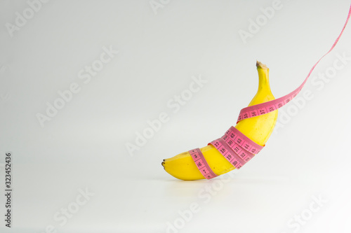 Close up of yellow ripe banana with body tape measure on white background. Healthy fruit concept.
