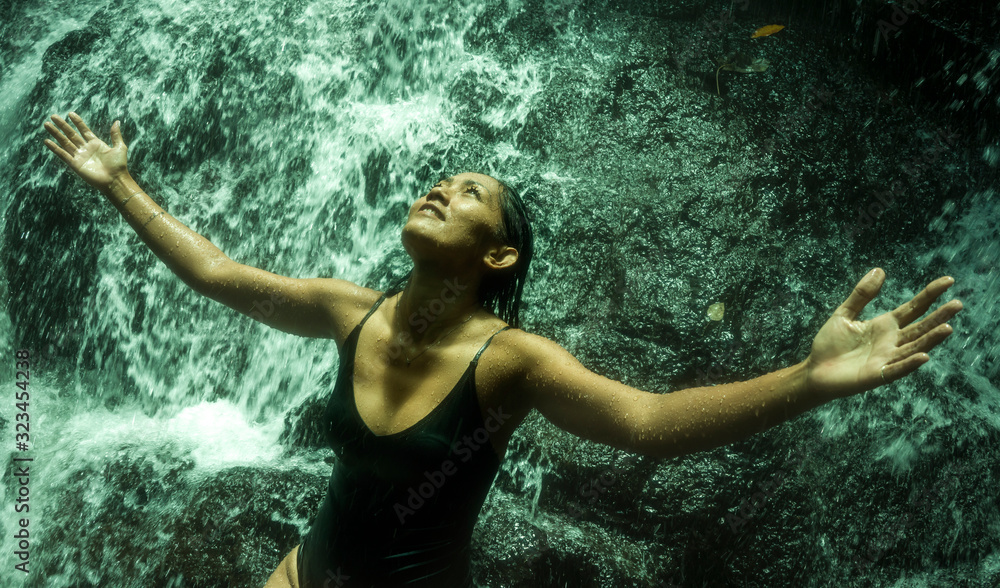Fototapeta premium young attractive and blissful Asian Indonesian woman overwhelmed by the beauty of natural waterfall in tropical jungle enjoying happy the amazing and exotic travel destination