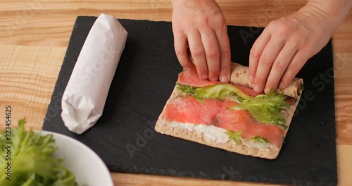 Woman making Swedish salmon, soft cheese, and lettuce roll for a lunchbox
