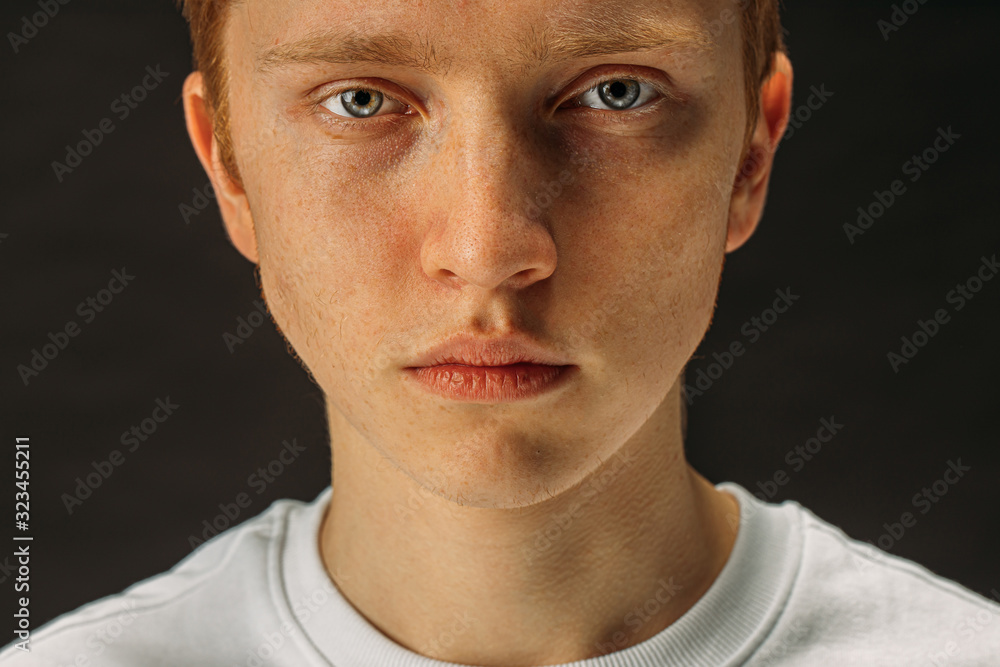 Obraz premium close-up face of caucasian redhaired boy seriously looking at camera, confident male in white shirt has piercing gaze, isolated black background
