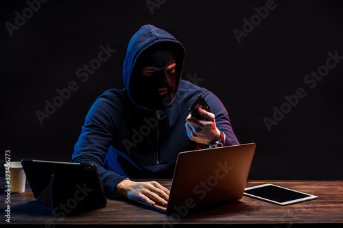 hacker male use laptop to gain unauthorized access to data, isolated in dark space. person in pullover with high knowledge of specific technology field, intervenes premeditatedly in different systems