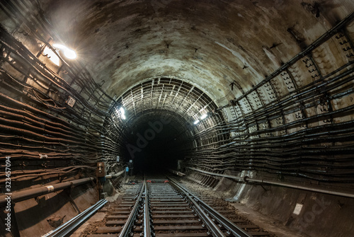The connection of a reinforced concrete tunnel with a cast-iron tunnel.The light is on.The connection of two metro railway tracks.High-voltage cables run along the walls
