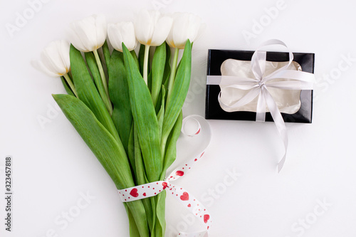 White tulip flowers and black gift box on light background flat lay. Place for text 8 March Happy Womens Mothers Day. Flower Bouquet with heart ribbon  greeting card.Copy space website banner top view