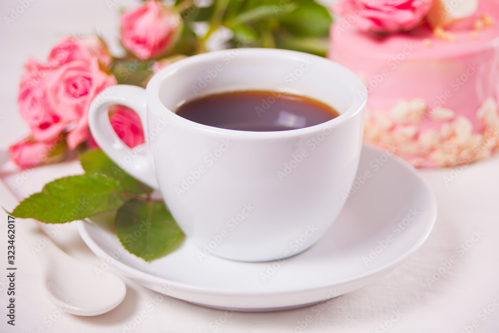 A cup of tea, pink roses and small cake on the white table A cup of tea, pink roses and small cake on the white table