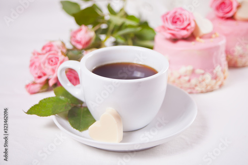 A cup of tea, pink roses and small cake on the white table